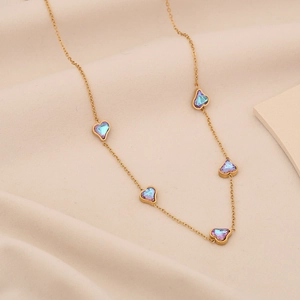 Dettaglio di collana dorata con ciondoli a cuore sfumati blu e viola su tessuto beige