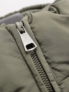 Detailed macro view of matte metal zipper and olive green textured fabric on hooded jacket