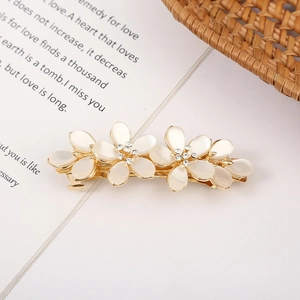 Macro detail of a golden flower hair clip with white petals and sparkling rhinestones