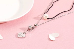 Detail of silver double-layered necklace with Love heart pendant, G charm and pearl