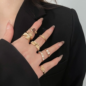 Detail of gold resin ring set with pearls and brown gemstones on hand over black suit