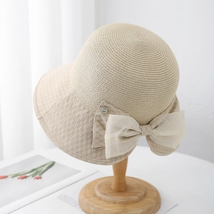 Detail of beige straw sun hat featuring a delicate tulle bow and small metal pendant