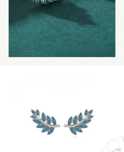 Macro shot of silver leaf earrings with turquoise stones on green velvet and white background
