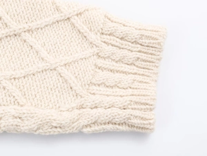 Detail der dicken cremefarbenen Zopfmusterstrickung und des Rippbündchens der Jacke