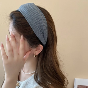 Detail eines hellgrauen breiten Strickstirnbandes mit eleganter vertikaler Rippstruktur