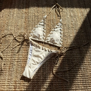 Detail of cream silk bikini with metal eyelets and khaki drawstring on straw mat
