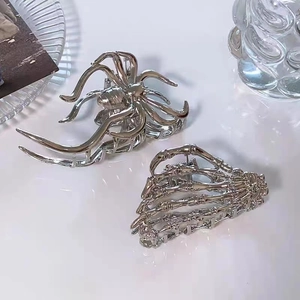 Polished silver metal hair claws in spider and skeleton hand designs on white surface