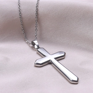 Detailed view of a silver stainless steel cross pendant on light silk fabric background