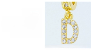 Macro detail of hand-set zircon on golden letter D pendant with diamond-cut finish