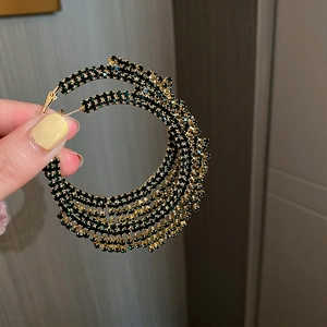 Detail von großen mehrlagigen Gold- und Grün-Strass-Creolen in der Hand gehalten
