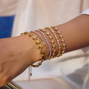 Detailed close-up of 18K gold-plated star and pink zircon layered bracelets on model wrist