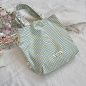 Detail of light blue plaid canvas tote bag with white lace handle and brand label