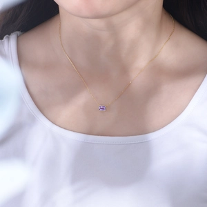 Close-up of elegant gold chain with rectangular purple amethyst pendant on a female neck