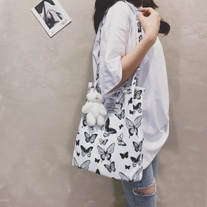 Detail of white canvas tote bag with black butterfly prints and a plush bear pendant