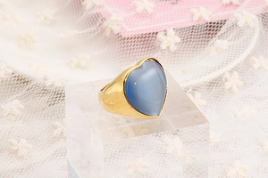 Detail of a gold heart ring with a blue gemstone on a crystal block with pink flowers