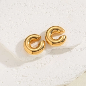 Macro shot of polished gold-plated C-shape hoop earrings on a textured stone surface