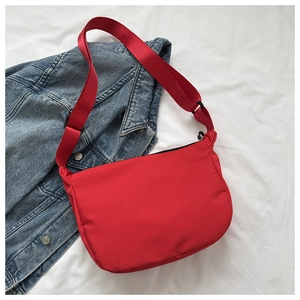 Flat lay of a red nylon crossbody bag with matching wide strap on denim jacket background