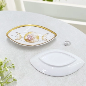 Close-up of white ceramic evil eye jewelry tray with gold rim and moon phases design