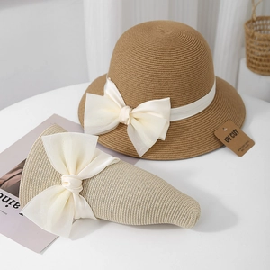 Détail de chapeaux en paille pliables avec grands nœuds blancs et étiquettes anti-UV
