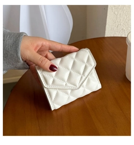 Close-up of a white quilted faux leather handbag with diamond pattern held in hand