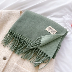 Detail shot of green faux cashmere scarf with tassels on a beige coat surface
