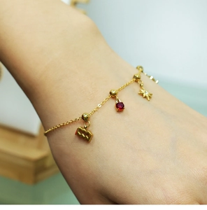 Detail of 18K gold bracelet with red gemstone, star and bar charms on a model's wrist