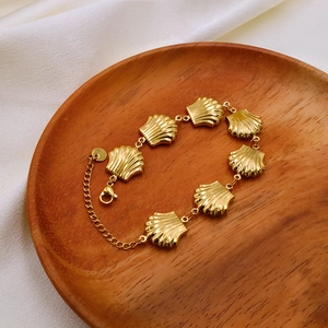 Detailed top view of a gold shell link bracelet on a wooden tray with silk background