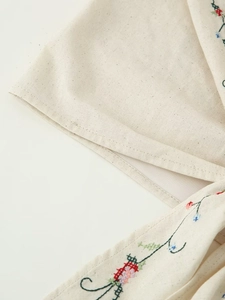 Vue macro de broderie florale colorée et coutures fines sur haut en lin beige