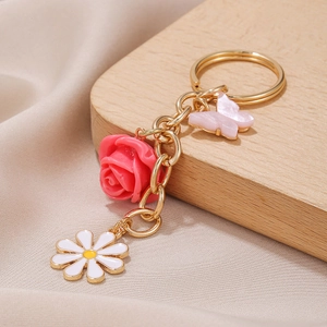 Golden daisy and pink rose flower pendant keychain on a light wood and fabric background