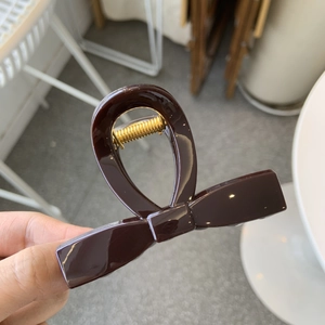 Detail of a dark brown bow-shaped hair claw clip with a glossy finish and gold metal spring