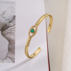 Detailed shot of gold evil eye cuff bracelet with green stone and wheat ear texture