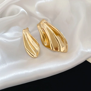 Macro detail of asymmetric gold fishtail earrings with organic wave texture on satin