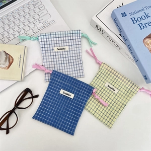 Three assorted plaid drawstring storage pouches with woven labels on office desk