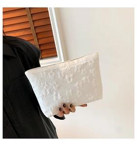 Close-up of white clutch bag with embossed 3D flower pattern texture held by a model