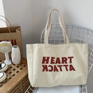 Detail view of the cream canvas tote bag with red Heart Attack lettering on a chair