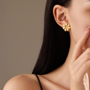 Close-up of elegant gold flower stud earrings with pearl accents on a female model