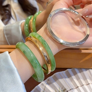 Stacked emerald green resin bangles with gold and silver metal rings on a wrist
