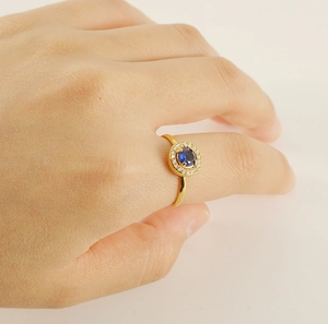 Close-up of a gold-plated halo ring with a round blue sapphire zircon on a model's hand