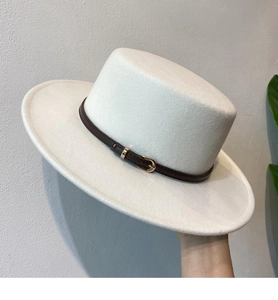 Detail of the white flat top felt hat with a brown leather buckle strap and metal pin