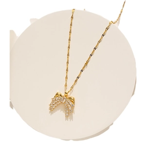 Elegant gold bow necklace with sparkling crystals on a minimalist white display
