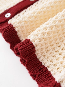 Detailed close-up of hollow crochet knit texture with red trim and pearl buttons