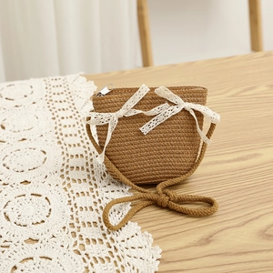Detail of children's straw crossbody bag with white lace bows on a rustic wooden background
