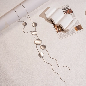Detail of silver long tassel necklace featuring round metallic discs on geometric props