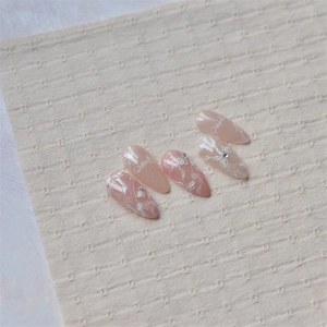 Detail of pink almond nails with white floral patterns and crystal accents on linen