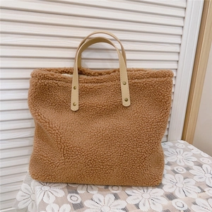 Detail of brown faux shearling tote bag with leather handles on a lace tablecloth