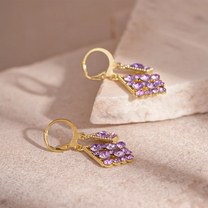 Detail of luxury gold earrings with pave-set purple rhinestones on a textured stone surface