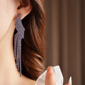 Macro detail of purple rhinestone geometric fringe earrings hanging on a model