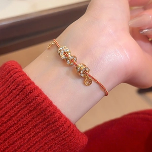 Gros plan d'un bracelet de pièces plaqué or avec corde tressée rouge et zircons
