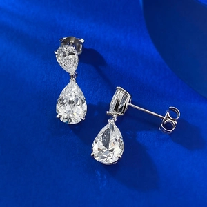 Macro shot of silver teardrop earrings with sparkling white zircons on a blue texture