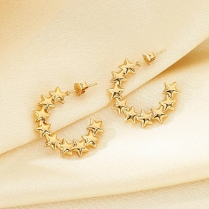 Detailed close-up of gold star hoop earrings resting on elegant beige silk fabric